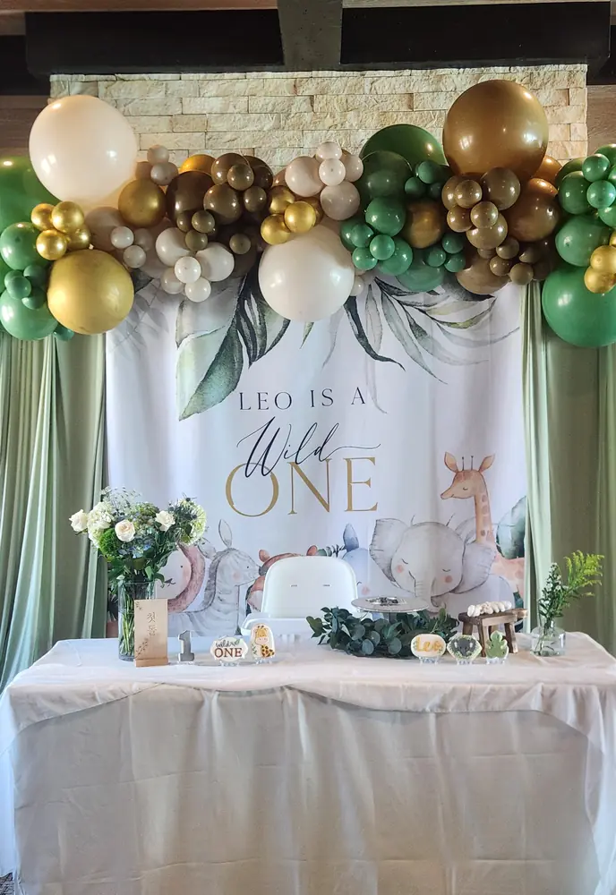 Green, gold, and ivory organic balloon garland over a Wild One first-birthday backdrop