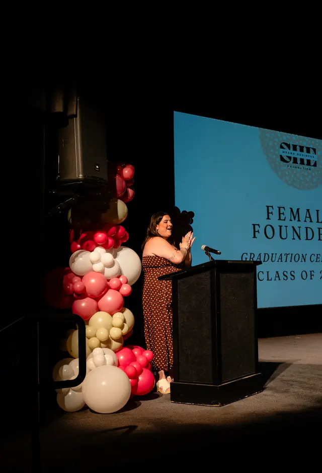 Pink, red, and cream organic balloon column beside the stage at a Female Founders graduation ceremony